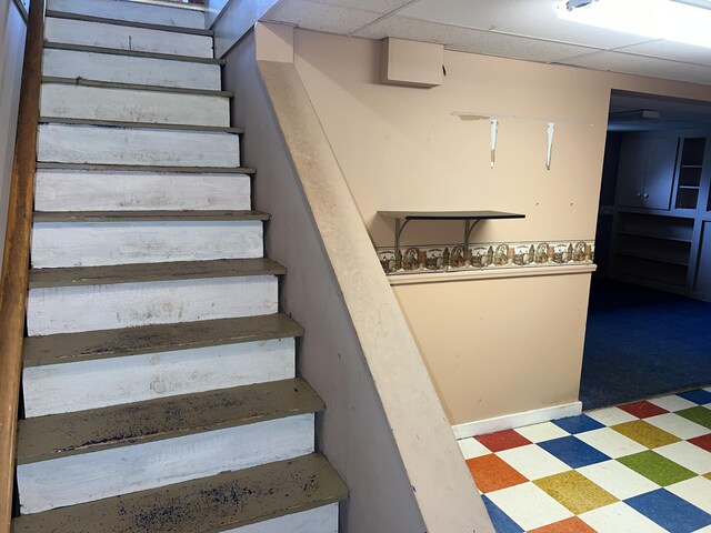 staircase featuring tile patterned floors and a paneled ceiling