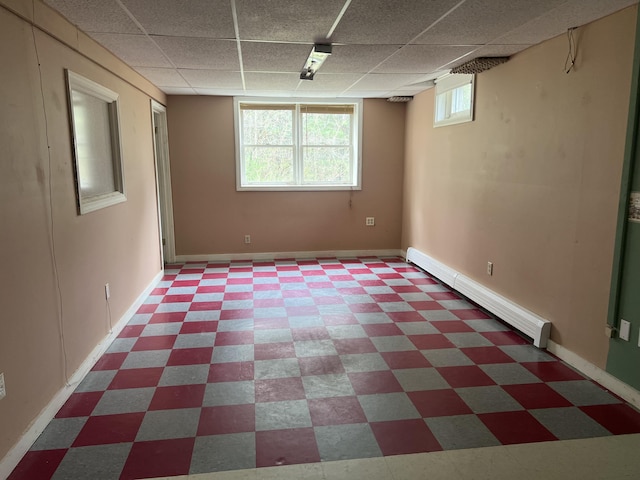 basement featuring a drop ceiling, tile patterned floors, and a baseboard heating unit