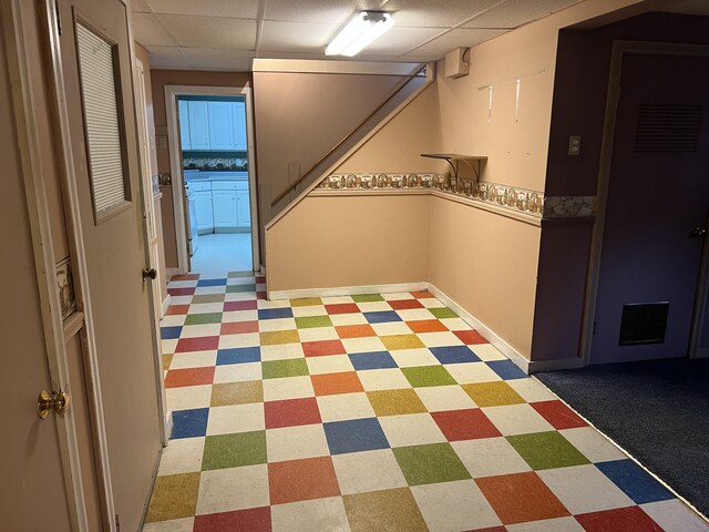 interior space with a paneled ceiling, light floors, visible vents, baseboards, and stairway