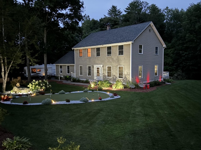 colonial-style house with a shingled roof, a front lawn, and a chimney