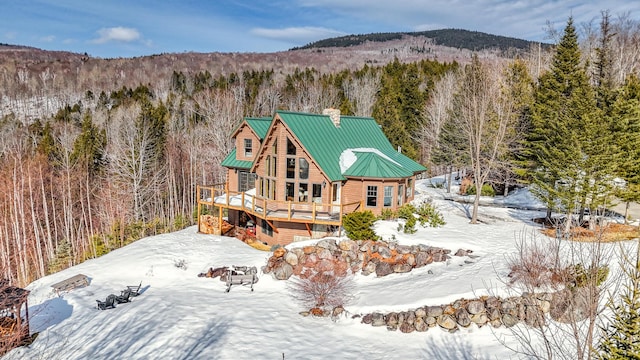 84 Ira Mountain Rd, Kingfield, ME 04947 - snow covered back of property featuring a chimney, a view of trees, a wooden deck, and a standing seam roof