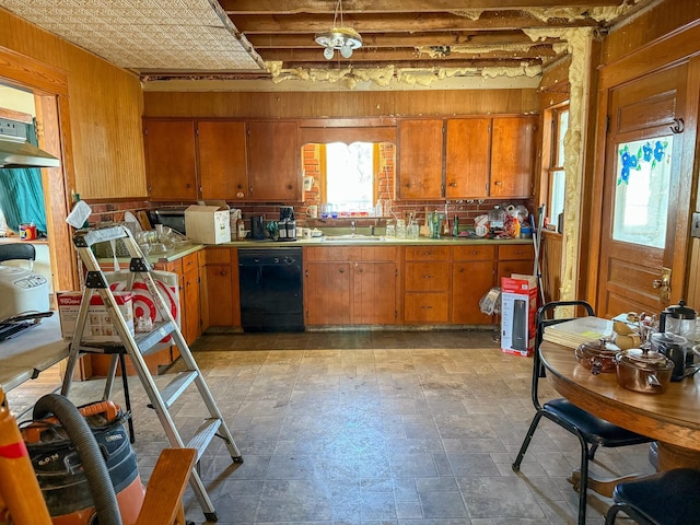 kitchen featuring brown cabinets, wood walls, light countertops, and black dishwasher