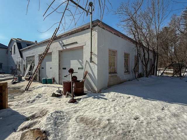 snow covered back of property with concrete block siding and a garage