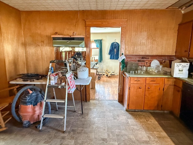 kitchen with dishwashing machine, wooden walls, brown cabinetry, and light countertops