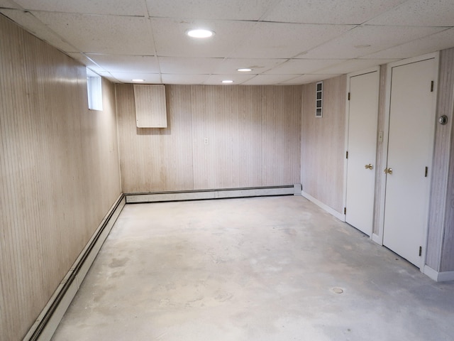 finished below grade area with a paneled ceiling, baseboard heating, and wood walls