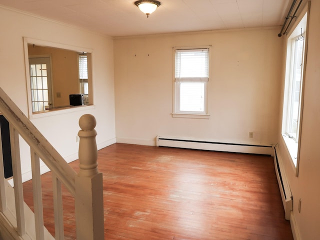 empty room featuring wood finished floors, baseboards, baseboard heating, and ornamental molding