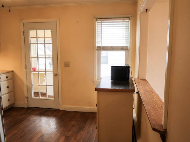 doorway with dark wood-style floors, baseboards, and ornamental molding