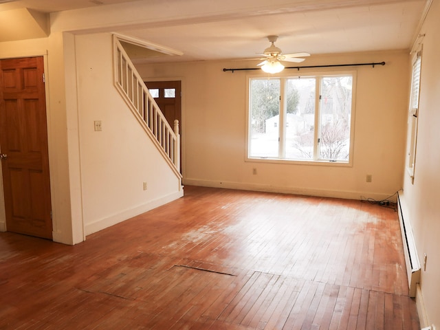 empty room featuring a baseboard heating unit, hardwood / wood-style floors, and stairs