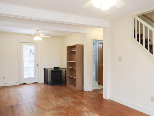 unfurnished living room featuring hardwood / wood-style flooring, stairway, a ceiling fan, and a wood stove