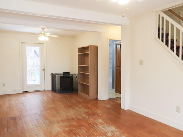 unfurnished living room with baseboards, stairway, a wood stove, a ceiling fan, and wood-type flooring