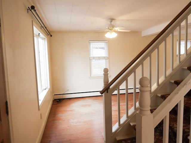 stairway with a baseboard radiator, wood finished floors, and a ceiling fan