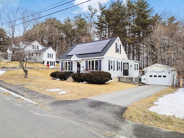 cape cod-style house with solar panels, aphalt driveway, roof with shingles, a garage, and an outbuilding