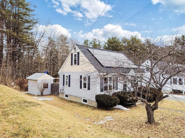 view of side of property featuring a shingled roof, roof mounted solar panels, a storage shed, an outdoor structure, and a yard