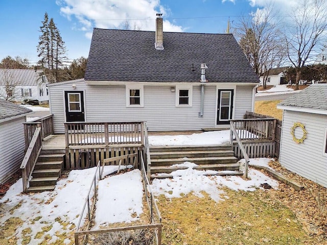 snow covered house with a shingled roof, a wooden deck, and a chimney