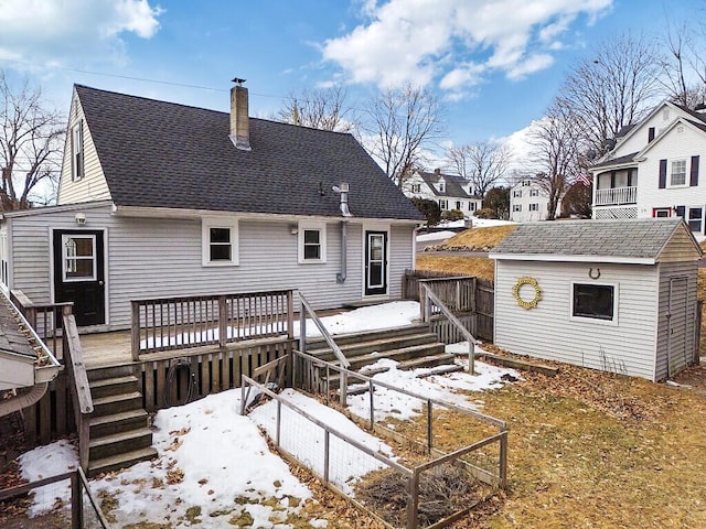 snow covered rear of property with roof with shingles, a chimney, a storage shed, a deck, and an outdoor structure