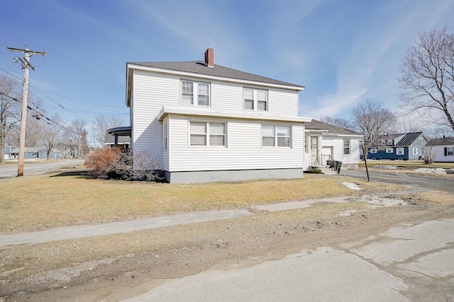 view of front of home featuring entry steps, a front lawn, roof with shingles, and a chimney