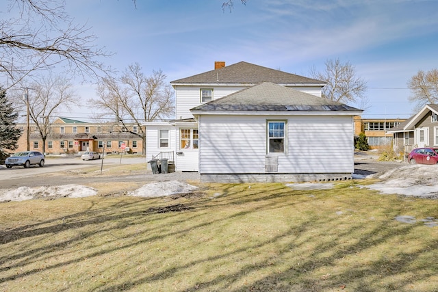 rear view of house featuring a lawn, entry steps, a chimney, and roof with shingles