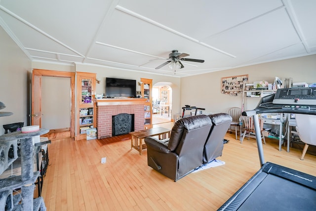 living room with arched walkways, a fireplace, a ceiling fan, and wood-type flooring