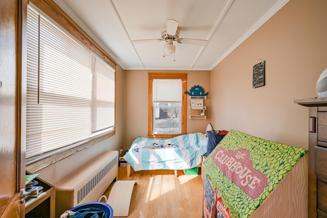 bedroom featuring a ceiling fan, wood finished floors, radiator heating unit, and crown molding