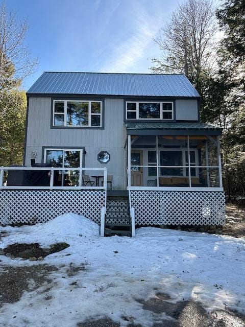 snow covered back of property featuring metal roof and a sunroom