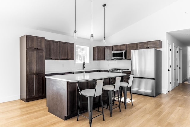 kitchen with a breakfast bar, light wood-style flooring, a kitchen island, stainless steel appliances, and dark brown cabinetry