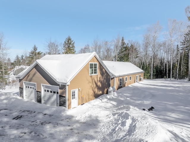 view of snow covered exterior featuring a detached garage and stone siding