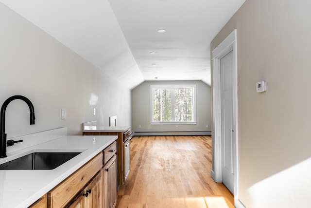 kitchen with light wood-type flooring, a sink, light countertops, lofted ceiling, and baseboard heating