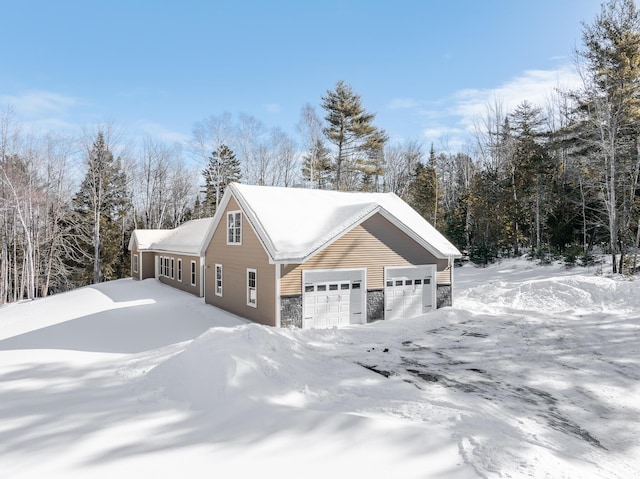 view of snow covered exterior featuring a garage and stone siding