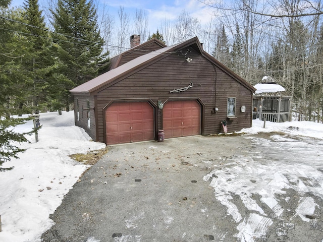 view of snowy exterior featuring aphalt driveway, a garage, and a chimney