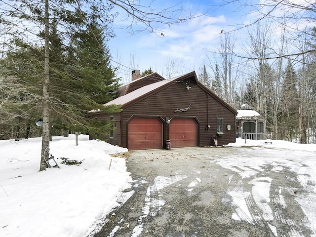 view of snow covered exterior featuring driveway, a chimney, a garage, and a sunroom