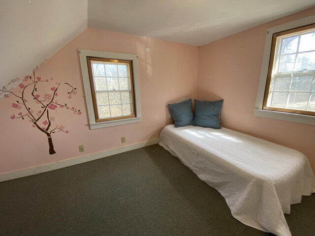 unfurnished bedroom featuring multiple windows, baseboards, dark carpet, and vaulted ceiling