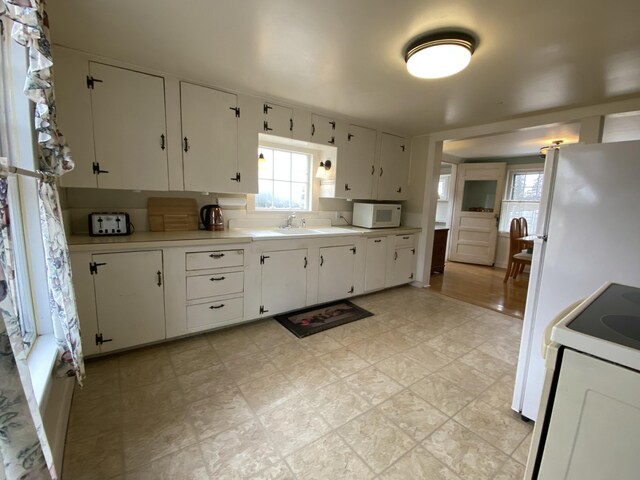 kitchen featuring plenty of natural light, white cabinets, and white appliances