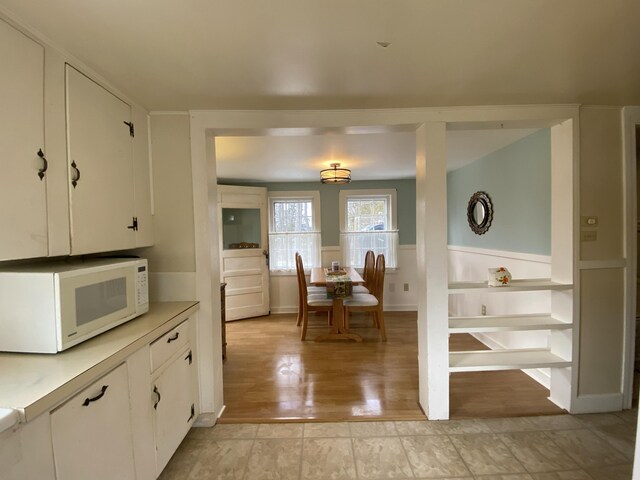 kitchen featuring white microwave, light countertops, light wood-style floors, wainscoting, and white cabinetry