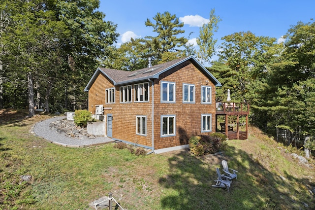 view of side of home with a wooden deck, a lawn, and a shingled roof