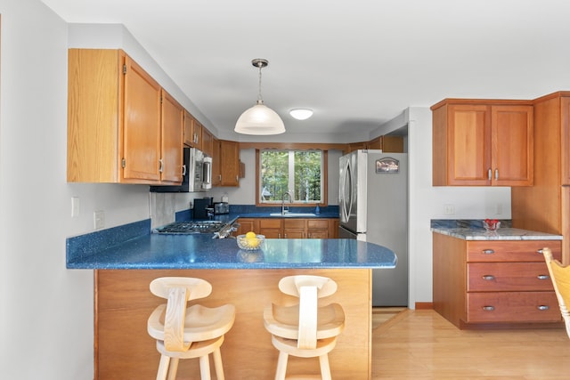 kitchen featuring appliances with stainless steel finishes, a sink, a peninsula, light wood finished floors, and pendant lighting
