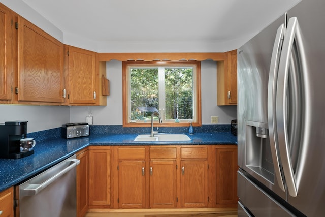 kitchen with stainless steel appliances, a sink, brown cabinetry, and dark stone counters