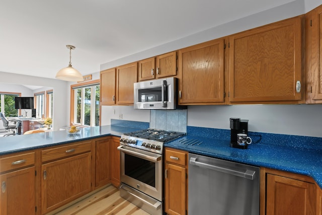 kitchen with appliances with stainless steel finishes, brown cabinetry, a peninsula, and dark countertops