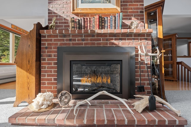 detailed view of a brick fireplace, carpet floors, and baseboard heating