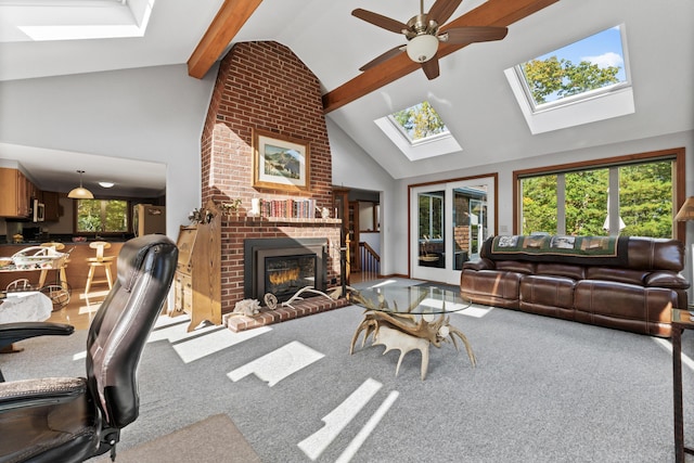 carpeted living room with a skylight, beamed ceiling, high vaulted ceiling, a brick fireplace, and ceiling fan