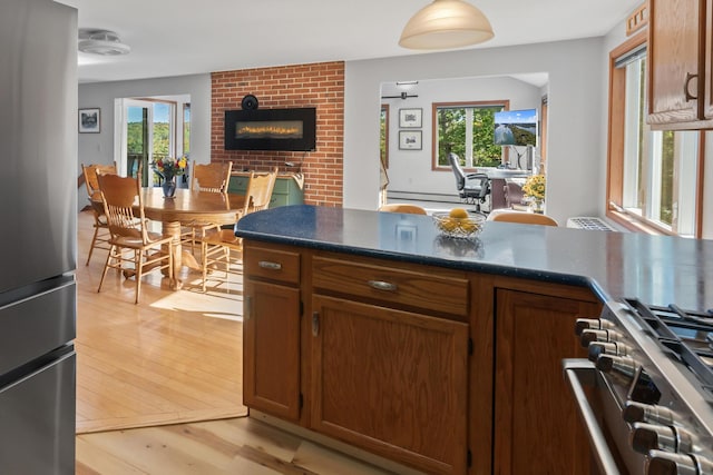 kitchen featuring stainless steel appliances, light wood-style floors, brown cabinets, dark countertops, and a fireplace