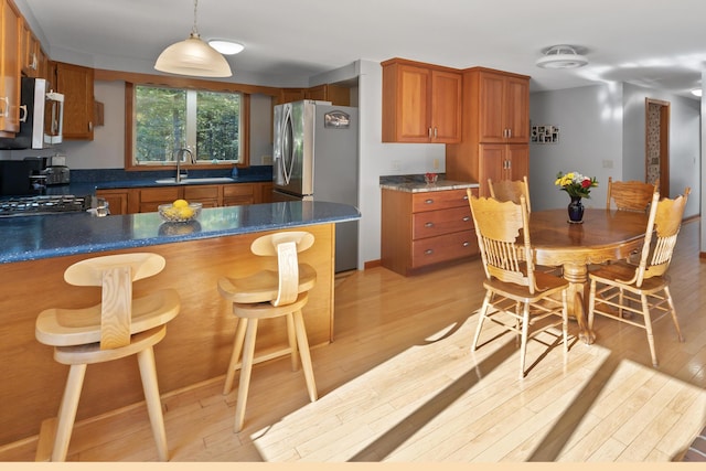 kitchen featuring appliances with stainless steel finishes, a sink, light wood-style floors, brown cabinets, and a peninsula