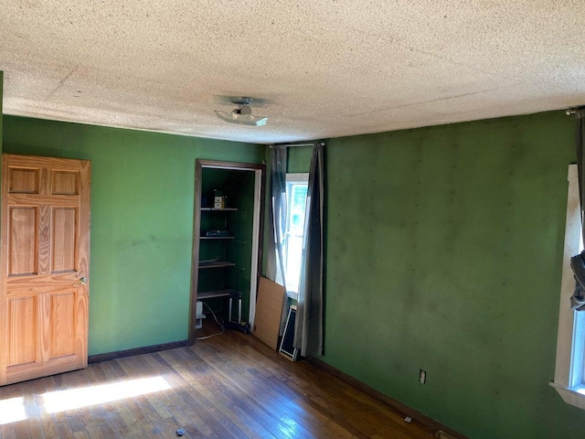 empty room with a textured ceiling, baseboards, and wood-type flooring