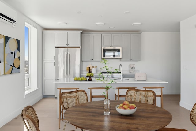 kitchen featuring a center island with sink, gray cabinets, a sink, stainless steel appliances, and light countertops