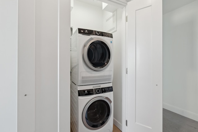 washroom featuring stacked washer / drying machine, baseboards, and laundry area