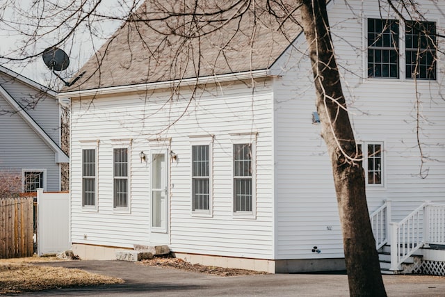 rear view of property with a shingled roof and fence