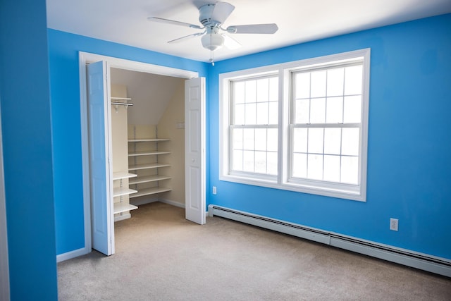 unfurnished bedroom featuring baseboard heating, multiple windows, a walk in closet, and carpet floors