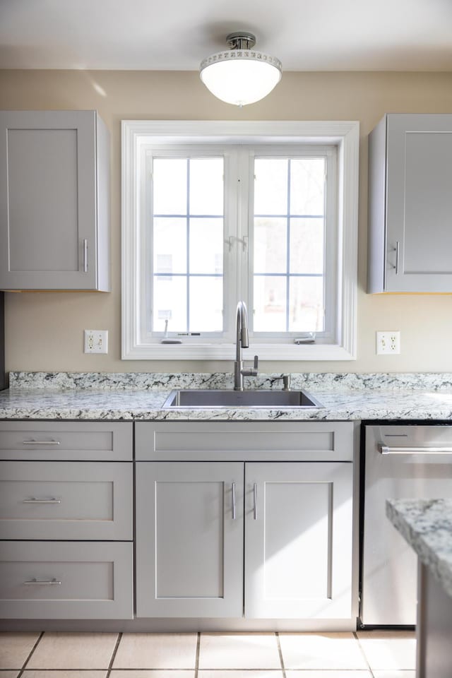 kitchen with gray cabinets, dishwasher, light stone countertops, and a sink