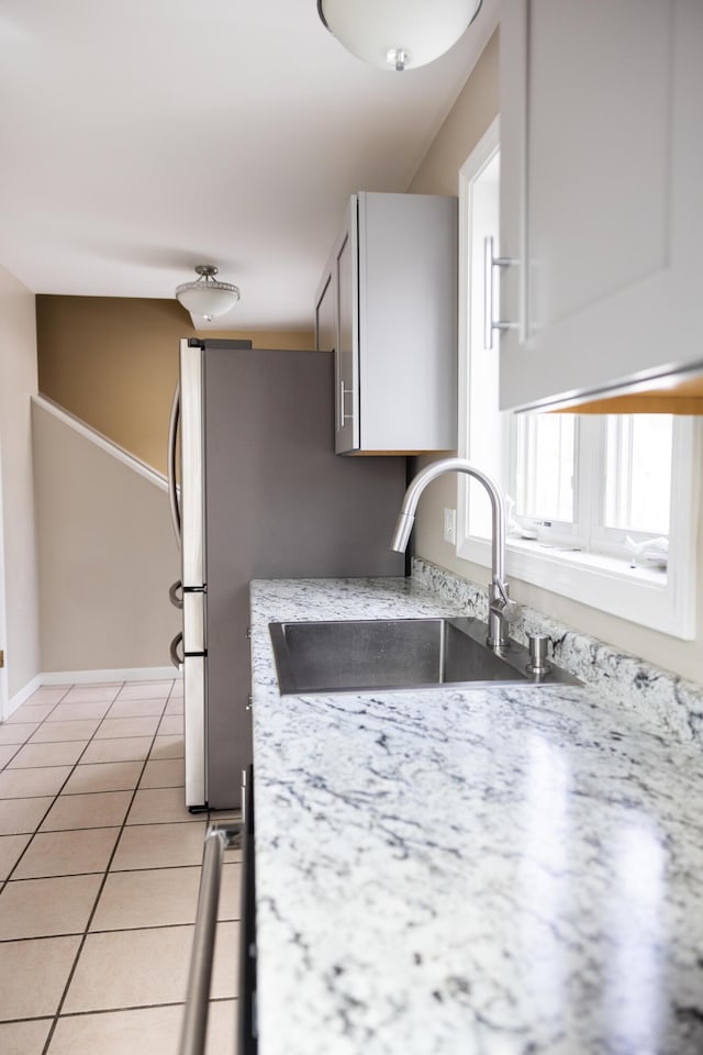 kitchen featuring light tile patterned floors, light stone counters, baseboards, and a sink