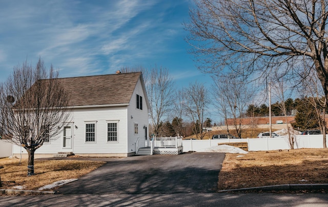 view of side of home featuring roof with shingles, fence, driveway, and a wooden deck