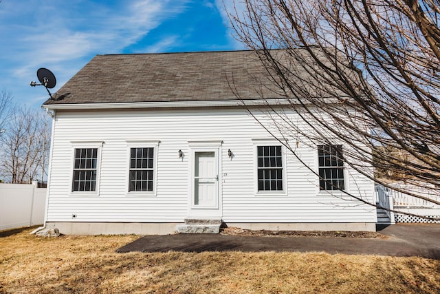 view of front facade featuring entry steps, roof with shingles, a front lawn, and fence